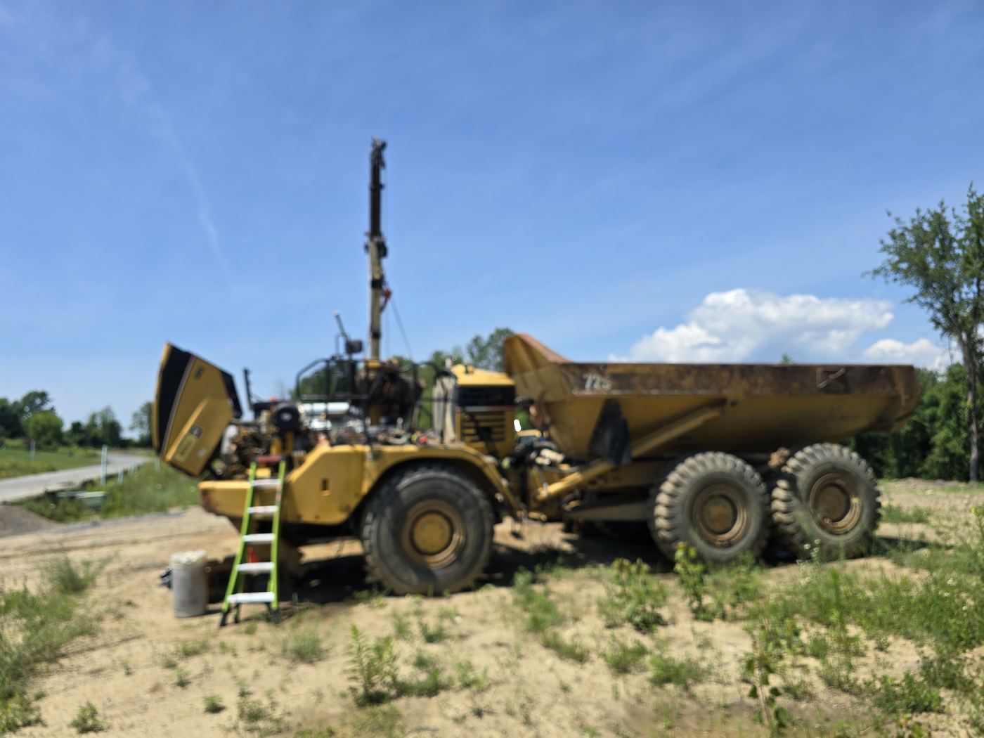CAT articulated dump truck with the engine hood open during an on-site repair at a job site