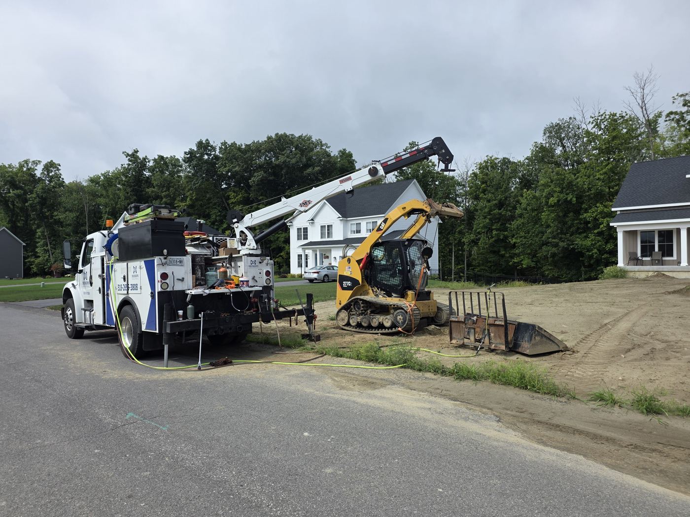 Decker's Industrial boom service truck with the crane extended, repairing a CAT 277C track loader at a residential job site