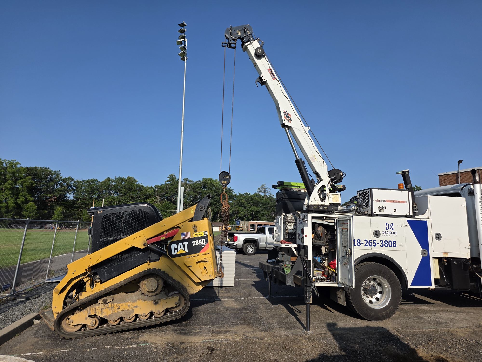 Decker's Industrial boom service truck lifting a component next to a CAT 289D track loader on a job site