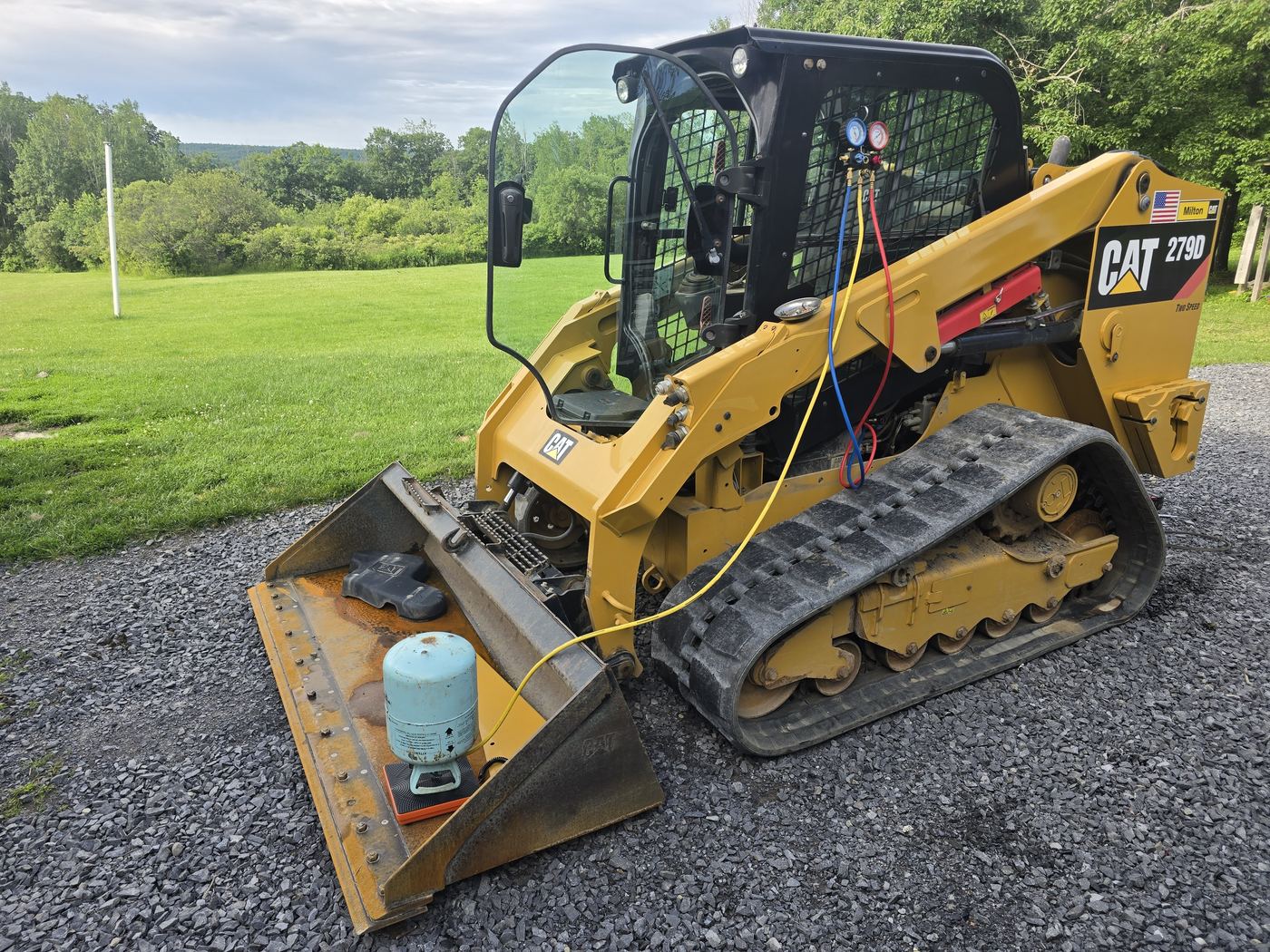 CAT 279D compact track loader in a field with the engine cover open during a scheduled preventative maintenance service